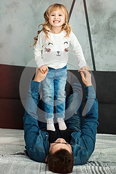 Vertical picture of dad and little smiling 3 years old daughter girl playing together in bed in bedroom. Family time on quarantine