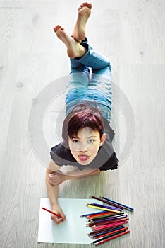 Vertical picture of drawing short haired mocking girl with pencils lying on floor. Idea how to spend time during quarantine in