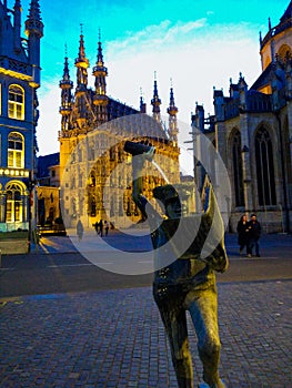 Vertical picture of Fons Sapientiae Fonske with the illuminated City Hall at the background in Leuven, Belgium