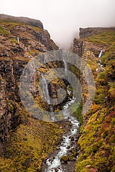 Vertical picture of the Glymur Waterfall surrounded by rocks covered in greenery and fog in Iceland