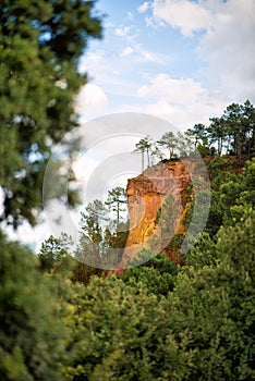 Vertical picture of hiking path Ochre Trail in a natural colorful area of orange cliffs surrounded by green forest in Roussillon,