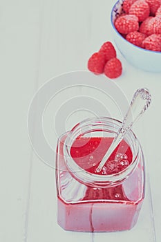 Vertical picture of raspberry jam in a jar with a spoon in it on the table near raspberries