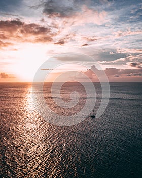 Vertical picture of a sea under a cloudy sky with the sun reflecting on it during sunset