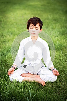 Vertical picture of short haired 7 years old girl in white kimono during meditation on karate training outdoors. Martial arts.