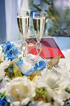 Vertical picture of wedding glasses with champagne, bride and groom rings and wedding decorations in summer sunny wedding day.