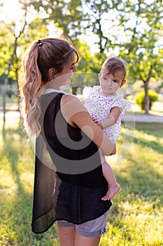 Vertical portrait against the background of nature of a cute barefoot baby in her motherâ€™s arms