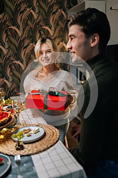 Vertical portrait of cheerful girlfriend making surprise, giving gift box with present to beloved young man on Christmas