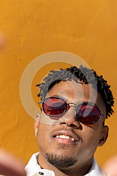 Vertical portrait close up black latino man with sunglasses smiling taking a selfie with his phone`s front camera