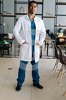 Vertical portrait of confident African American male doctor wearing medical lab uniform standing in hospital office
