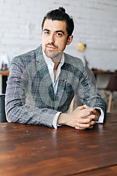 Vertical portrait of confident stylish business man in fashion suit sitting at desk in modern office room, looking at