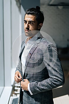 Vertical portrait of confident stylish business man wearing fashion suit standing in modern office room, looking out