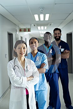 Vertical portrait of diverse group of smiling healthcare workers wearing cancer ribbons, copy space