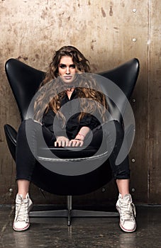 Vertical portrait of a domineering young woman sitting in the black chair photo