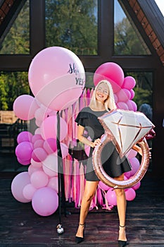 Vertical portrait of elegant blonde female in summer dress posing holding various colorful festive foil helium balloons