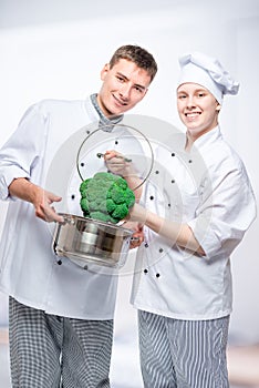 Vertical portrait of fellow cooks with saucepan and broccoli