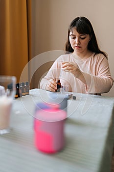 Vertical portrait of female artisan preparing using of scented oil for creating candle building mixture. Process of