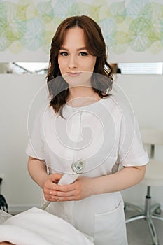 Vertical portrait of female beautician holding RF lifting apparatus for cosmological procedure, looking at camera