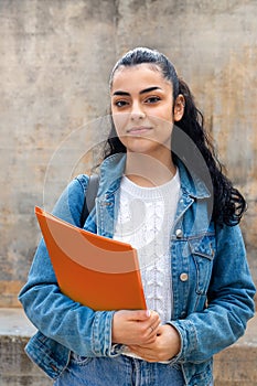 Vertical portrait of female caucasian college student looking at camera carrying folders and a backpack.