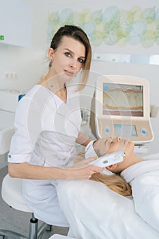 Vertical portrait of female cosmetologist making ultrasound face lifting massage with professional equipment for young