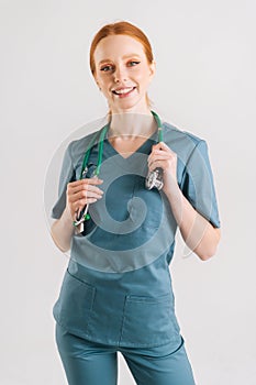 Vertical portrait of friendly young female physician in medical uniform with stethoscope around neck looking at camera,