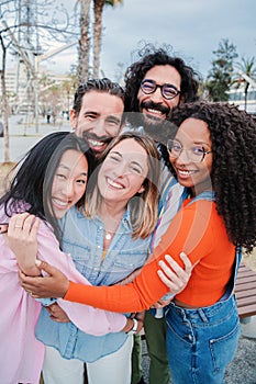 Vertical portrait of group of joyful young adult friends hugging each others. Happy smiling multiracial people embracing