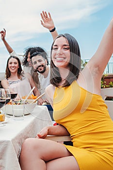 Vertical portrait of a group of young adult friends having fun and laughing on a dinner party rooftop. Happy multiracial