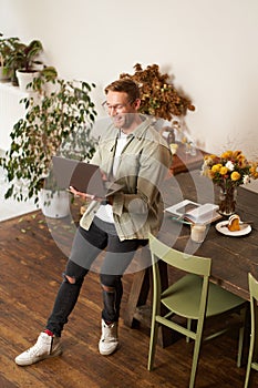Vertical portrait of handsome happy man, manager or CEO of company, sitting on table and holding laptop, laughing, video