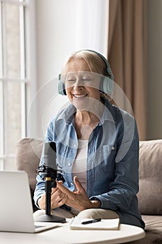 Vertical portrait happy 65s woman in headphones speaks into microphone