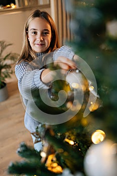 Vertical portrait of happy adorable little girl enjoying process of decorating Christmas tree at home. Cute smiling