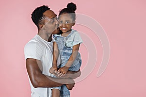 Vertical portrait of happy afro daddy embracing with his cute baby daughter, pink studio background.