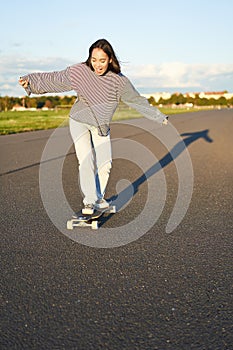 Vertical portrait of happy asian girl enjoying skateboard fun day out. Smiling korean skater on longboard, riding along