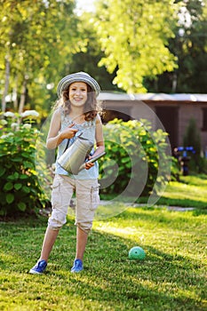 Vertical portrait of happy child girl in gardener hat playing with watering can