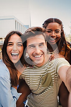 Vertical portrait of a happy multicultural friends laughing taking a selfie together. Mixed teenage cheerful students