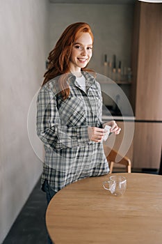 Vertical portrait of happy young woman opening bag with drip coffee standing at kitchen table in morning, smiling