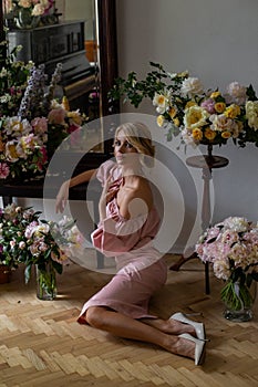 Vertical portrait indoors of a slender blonde surrounded by chic bouquets