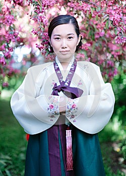 Vertical portrait of Korean woman in Hanbok national costume standing against blossoming sakura trees background in the spring photo