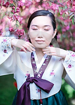 Vertical portrait of Korean woman in national hanbok costume with closed eyes poses for the camera, bringing her hands to the face photo