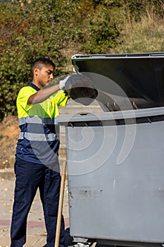 Vertical portrait of latin garbage man throwing garbage into dumpster in work clothes