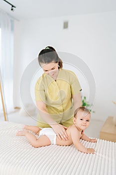 Vertical portrait of loving mother massaging little baby. Front view of adorable infant baby boy lying on belly while