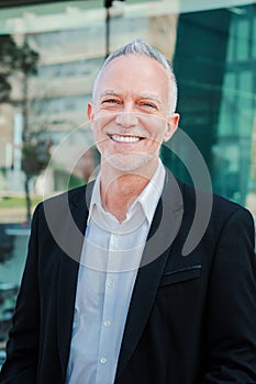 Vertical portrait of mature adult business man with gray hair and suit smiling and looking at camera with succesful