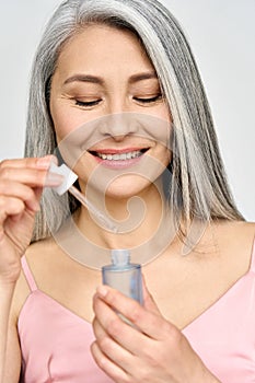 Vertical portrait of mature Asian woman holding pipette and bottle serum.