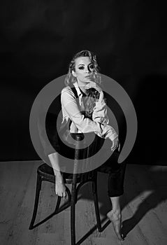 Vertical portrait of a pretty barefoot blonde sitting on a chair in the studio