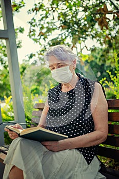 Vertical portrait of a senior adult woman in face mask reading a book.