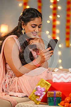 vertical shot ofaJoyful young Indian girl using mobile phone during Diwali festival celebration at home in front of