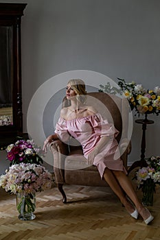 Vertical portrait of a slender blonde sitting in an armchair against a background of chic bouquets