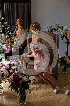 Vertical portrait of a slender blonde sitting in a chair near the mirror