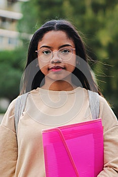Vertical portrait of smart young latin school girl holding the notebook with pensive attitude. Serious hispanic teenage