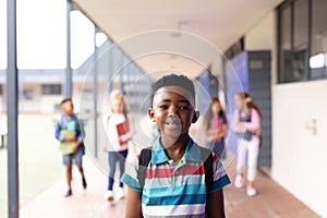 Vertical portrait of smiling african american boy in elementary school corridor, with copy space