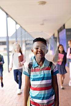 Vertical portrait of smiling african american boy in elementary school corridor, with copy space