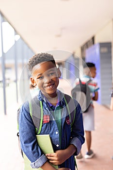 Vertical portrait of smiling african american boy in elementary school corridor, with copy space